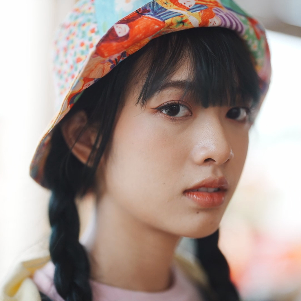 Close-up of young girl with braided pigtails and colourful hat looking at the camera