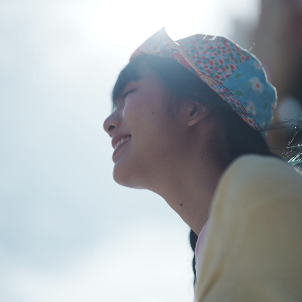 Close-up side view from bottom left of girl with colourful hat smiling 