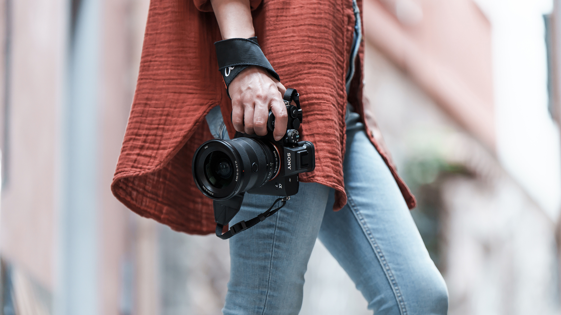 Man in red shirt and jeans walking with a Sony camera in his right hand